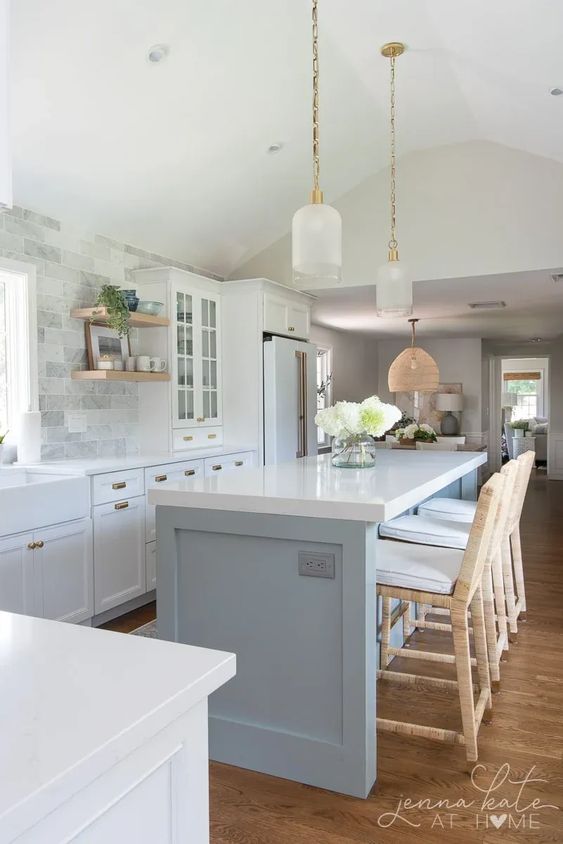 coastal grand millennial kitchen with light blue kitchen island and white kitchen cabinets. Gold accents, light wood floors, white marble backsplash.